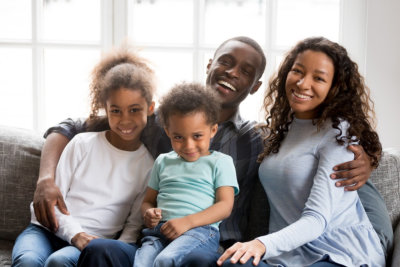 Portrait of happy large African American family at home sitting on couch together, smiling father embracing attractive wife and preschooler daughter