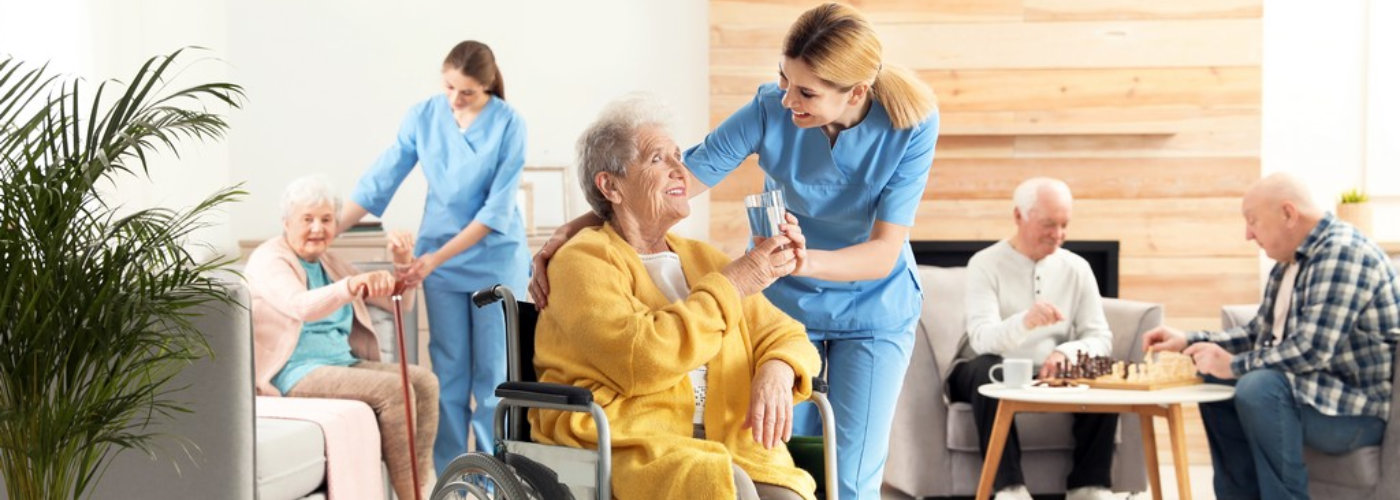 Nurse giving glass of water to elderly woman in wheelchair at retirement home.